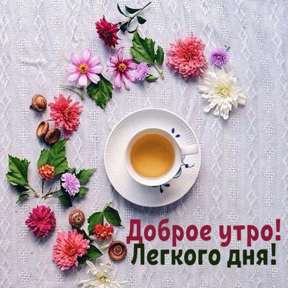 Чашка кофе среди цветов и листьев с надписью Доброе утро! Легкого дня! на столе с белым скатертью.