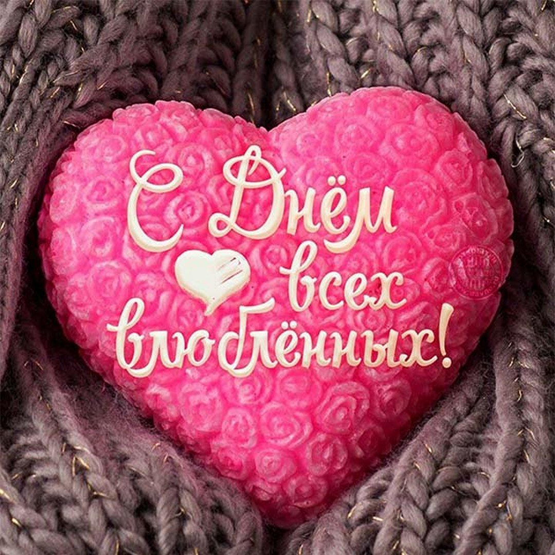 Розовое сердце с надписью С Днём всех влюблённых! на фоне коричневого вязаного узора.