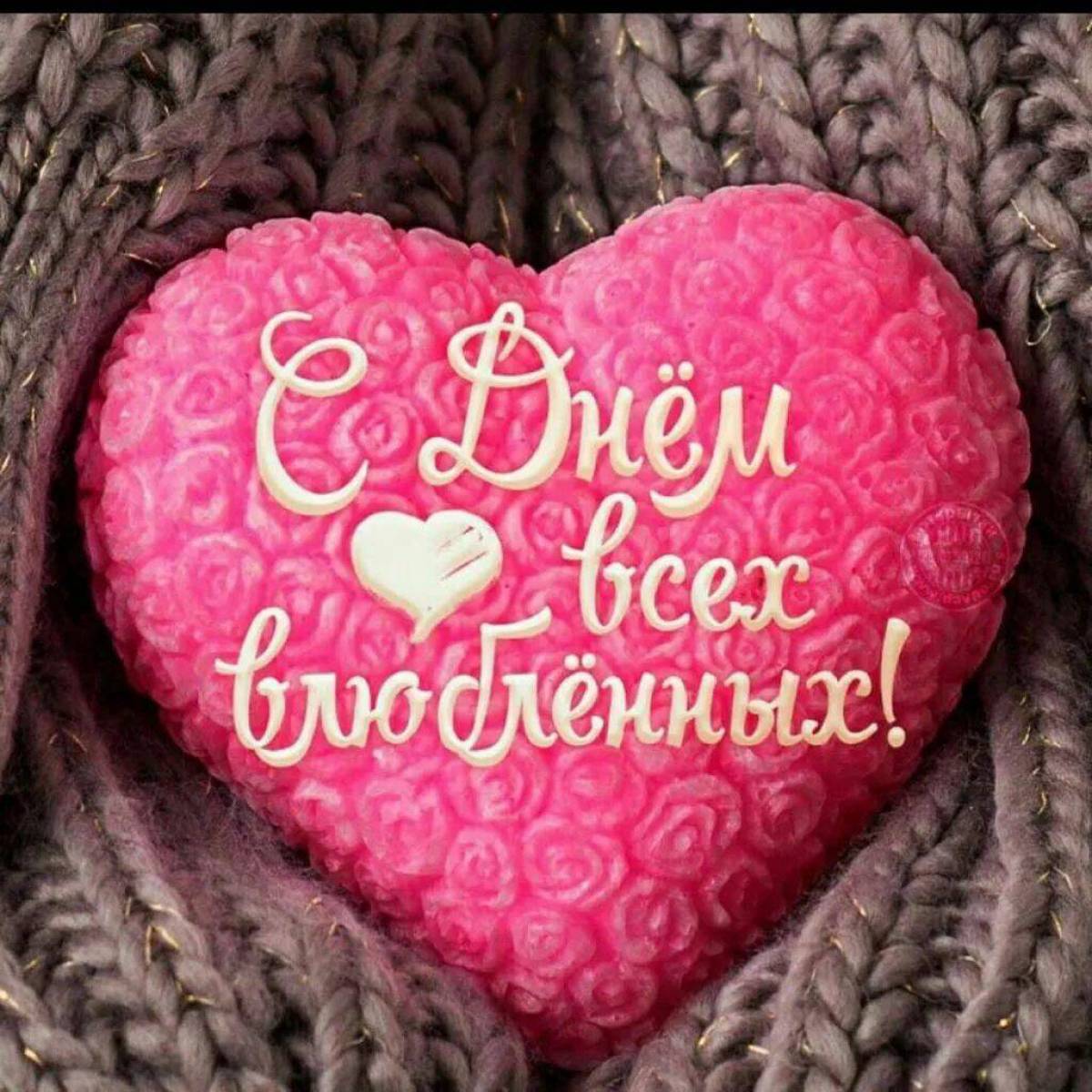 Розовое сердце с поздравлением С Днём всех влюблённых! на фоне тёмно коричневой вязаной ткани.